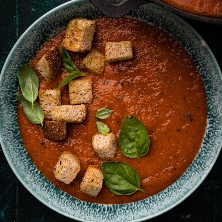 Bowl of creamy tomato soup with fresh basil and croutons on top.