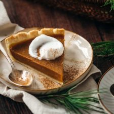 A slice of vegan pumpkin pie topped with whipped cream and a sprinkling of cinnamon.