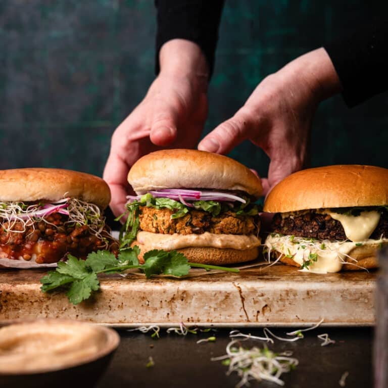 Three different type of vegan burgers on a tray. The one in the center is being picked up.