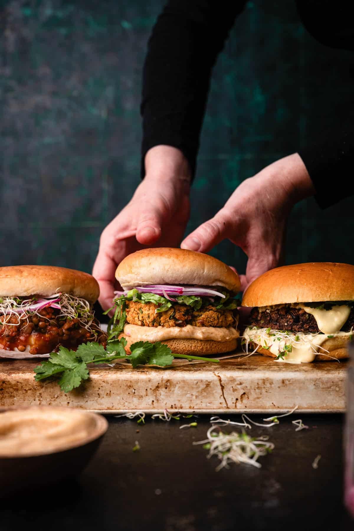 Three different type of veggie burgers on a tray. The one in the center is being picked up.