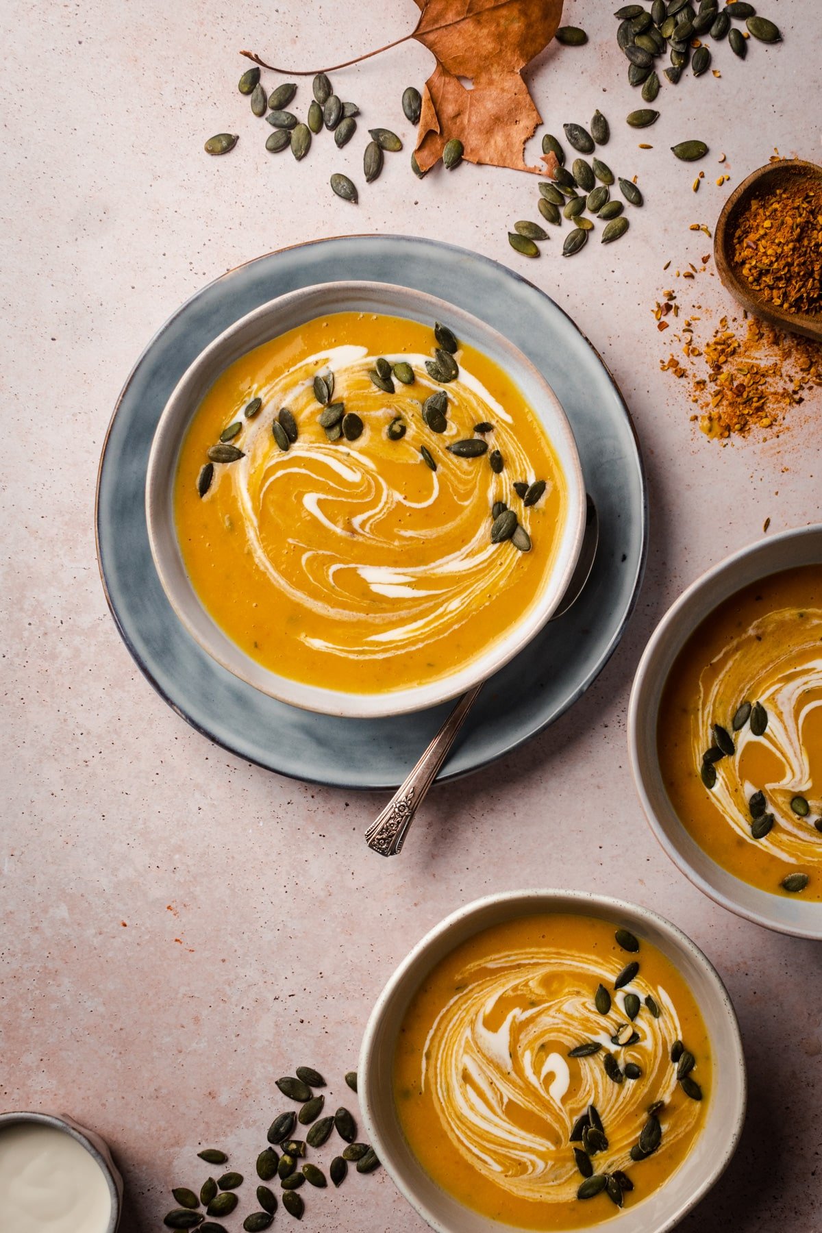 Three bowls of creamy soup with pumpkin seeds and fall leaves.