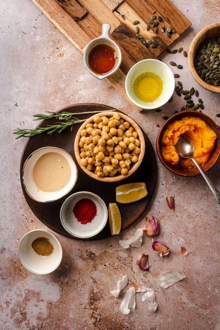 Black platter with chickpeas, tahini, spices, herbs, and pumpkin puree.