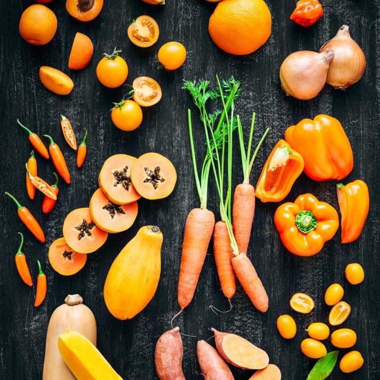 Butternut squash, carrots, oranges, and other orange fruits and vegetables on a black surface.