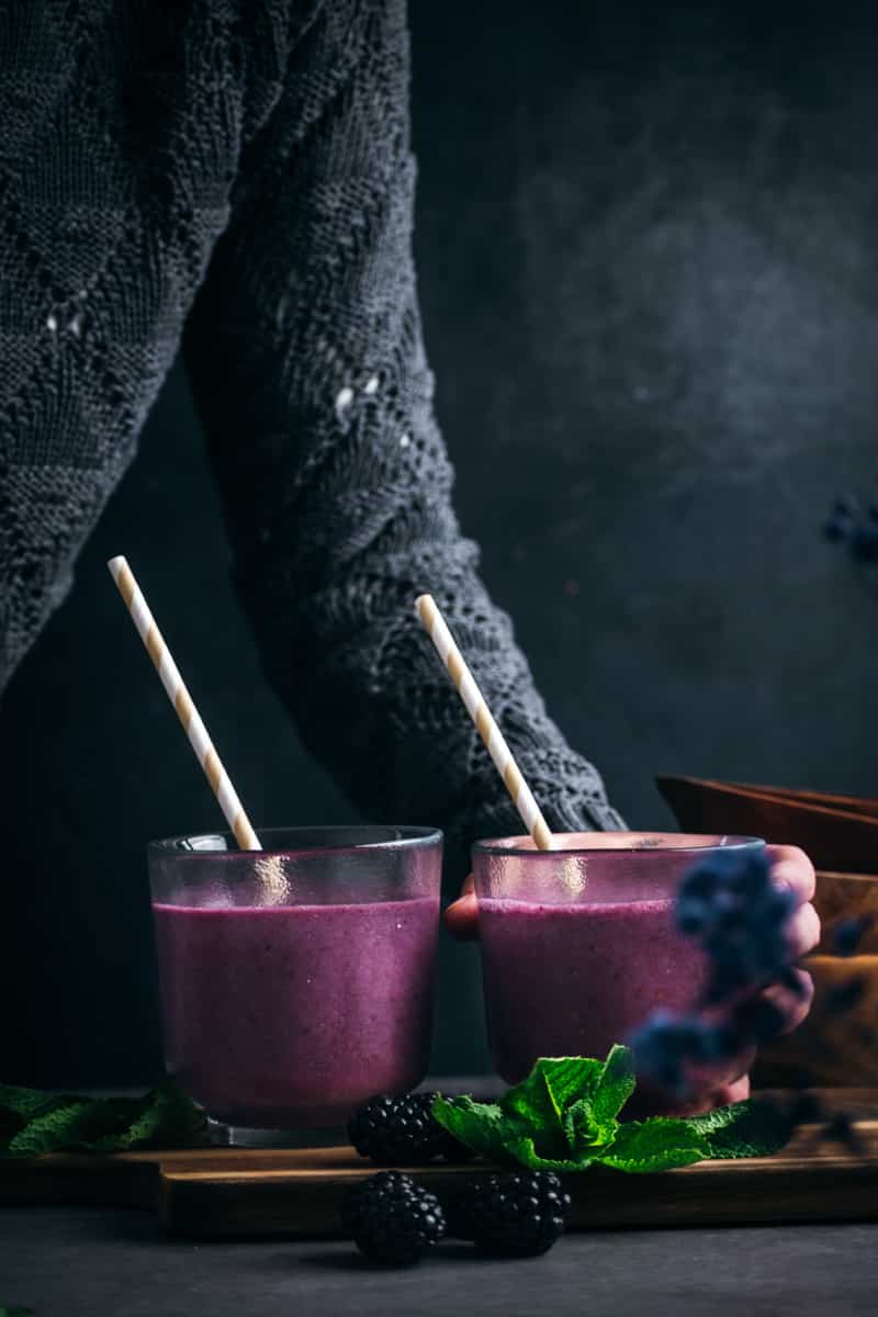 Two cups of dark purple smoothie with paper straws.