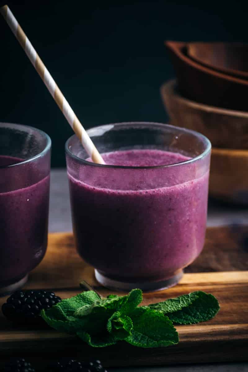 Short cup filled with deep purple blackberry smoothie with a paper straw.