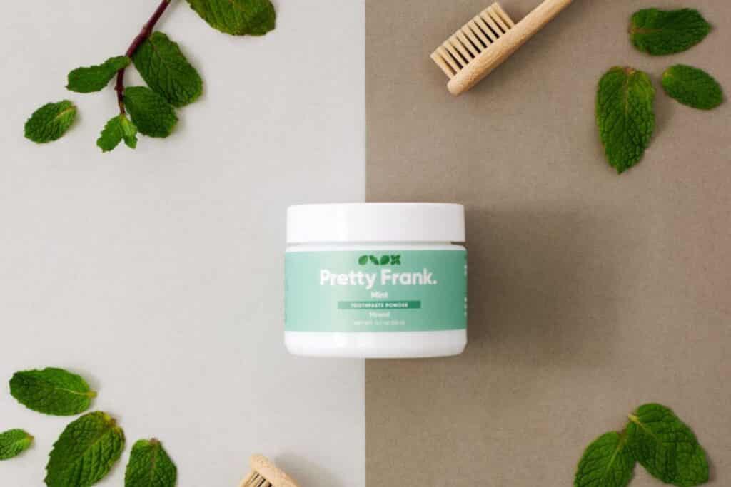 White glass jar with soft green label of low-waste toothpaste.