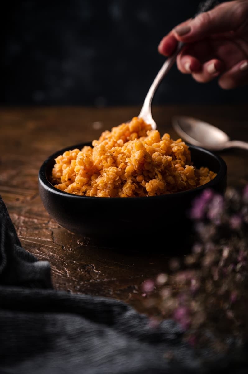 Cooked red lentils in a black bowl with a spoon scooping some out.