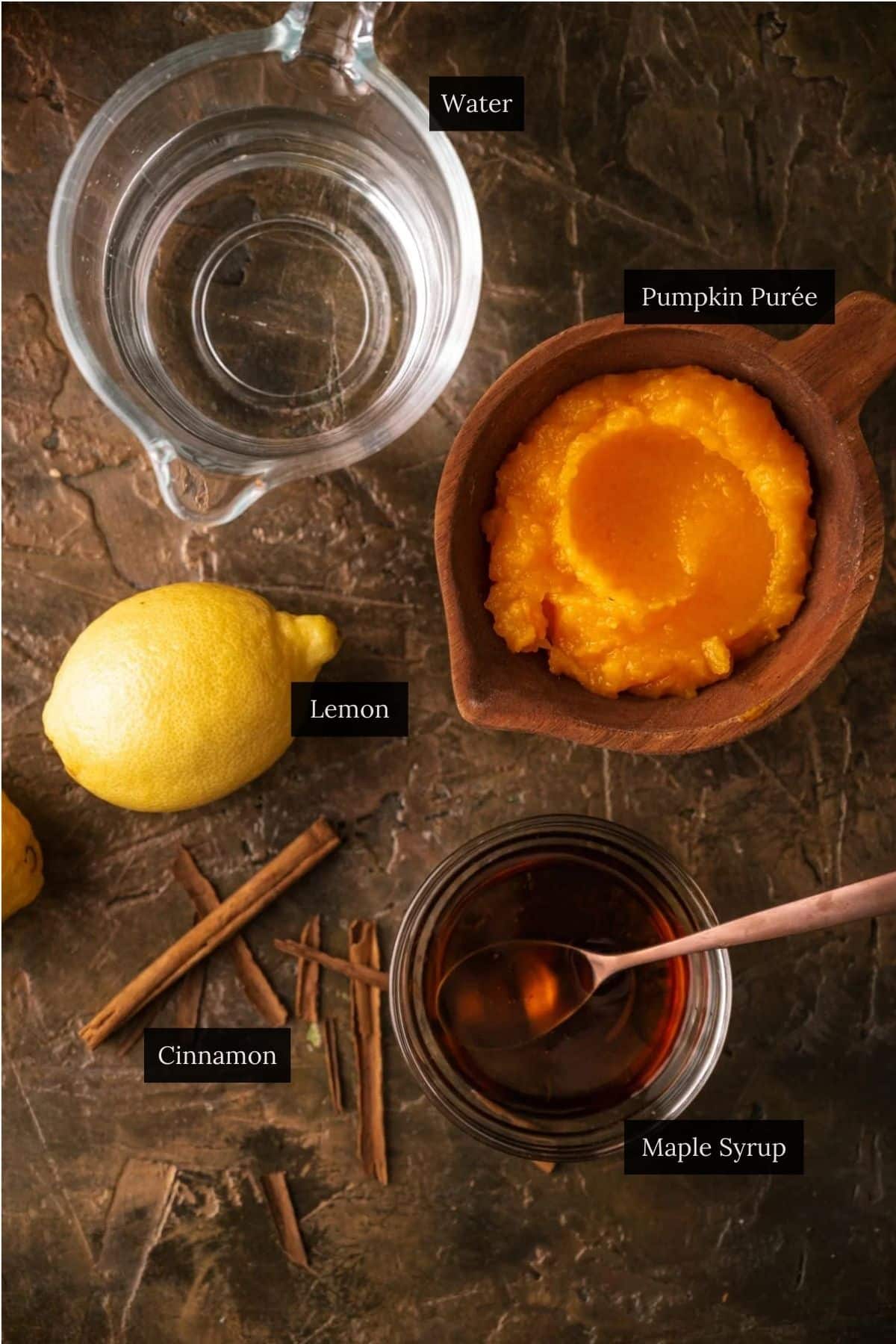 Ingredients on a table: a glass of water, a bowl of pumpkin purée, cinnamon, and a lemon ready to be squeezed. 