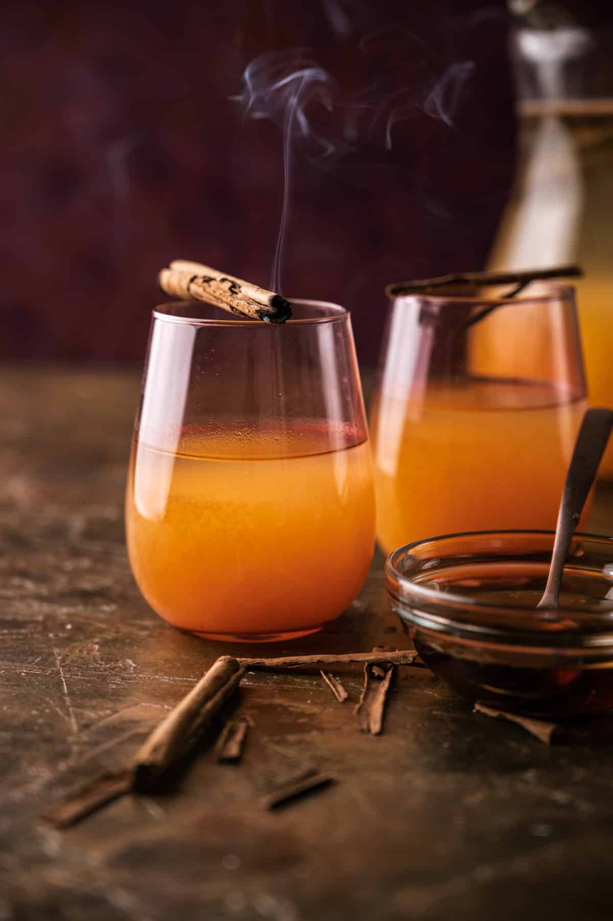 Two cups and a pitcher of pumpkin lemonade with smoking cinnamon sticks.