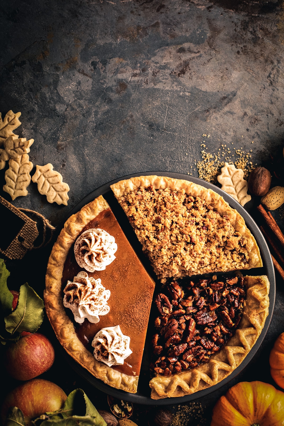 One third of three different pies put together in a pie pan with fresh fall produce around. 