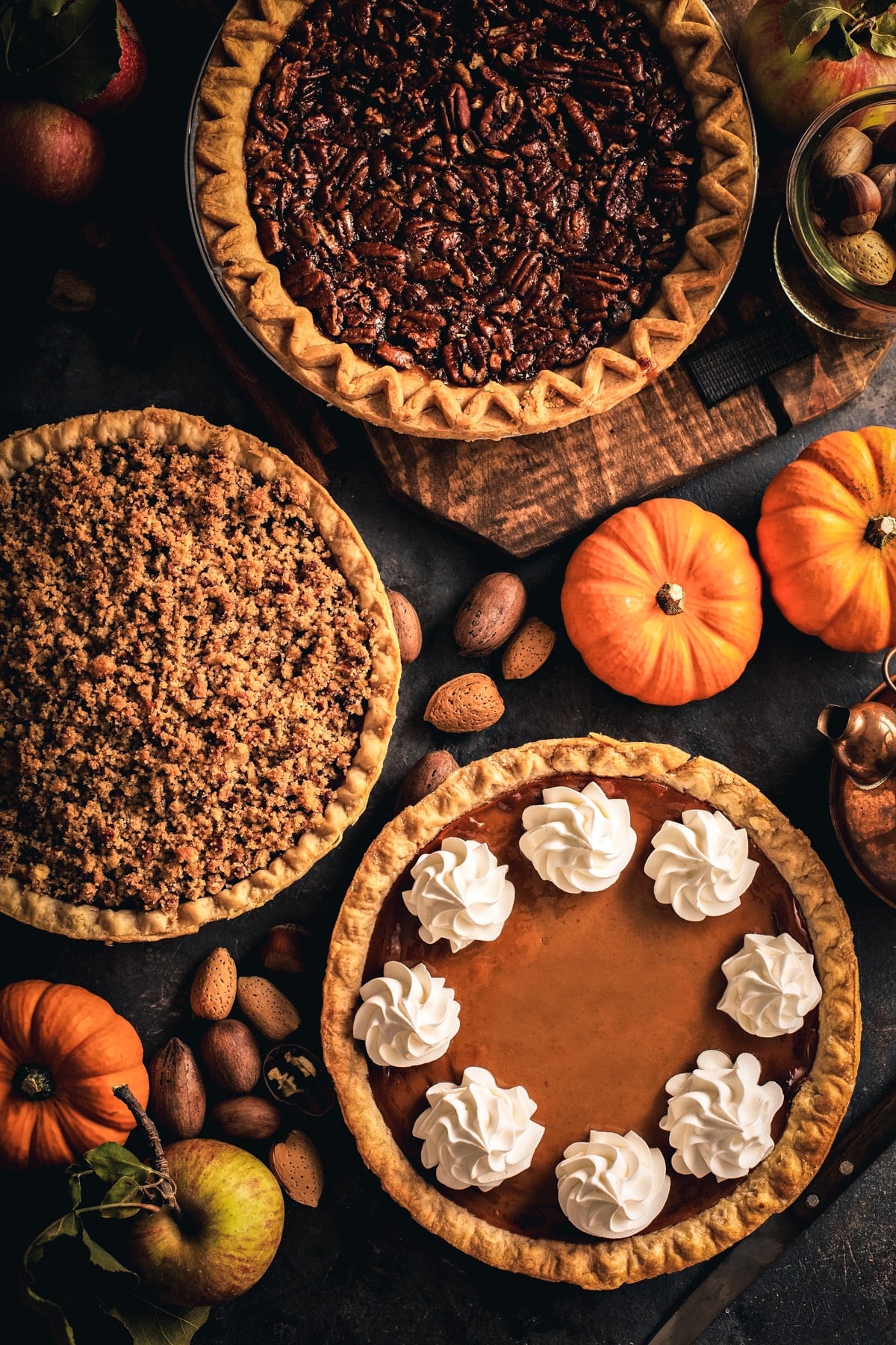 Three fall pies on a charcoal colored surface with pumpkins around. 
