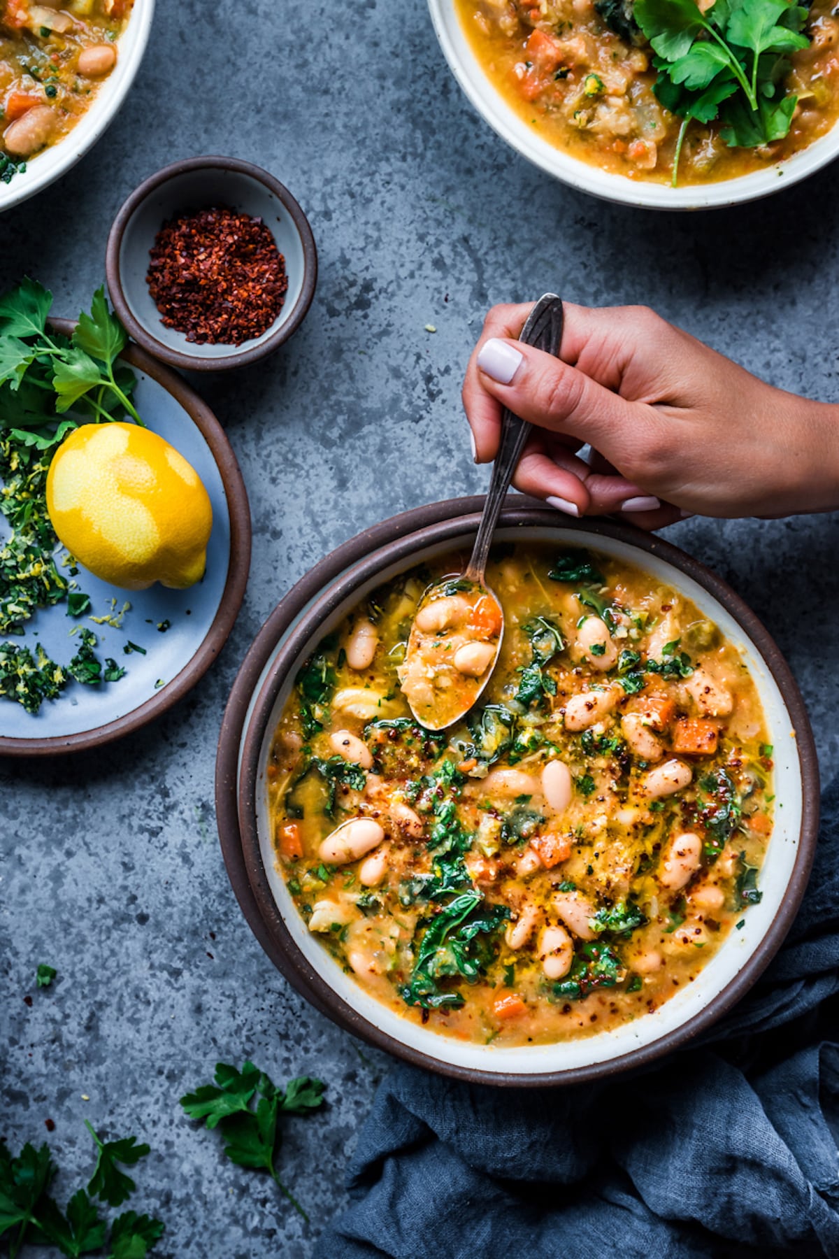 Bowl of white bean vegetable soup on a dark gray background.