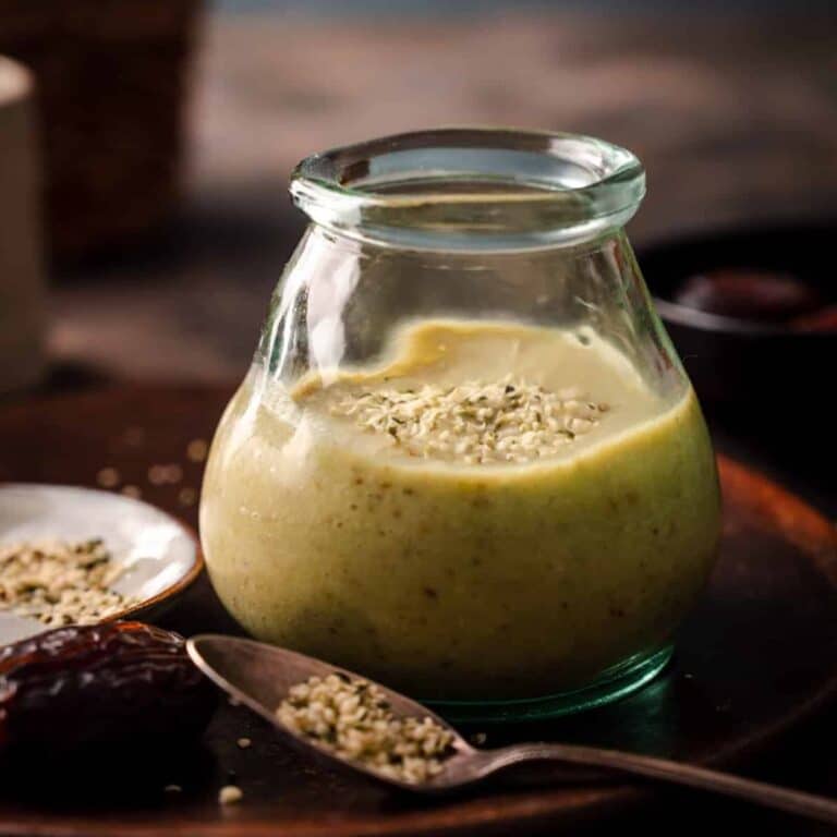 A small glass jar filled with avocado smoothie with a spoon of hemp seeds on the table.
