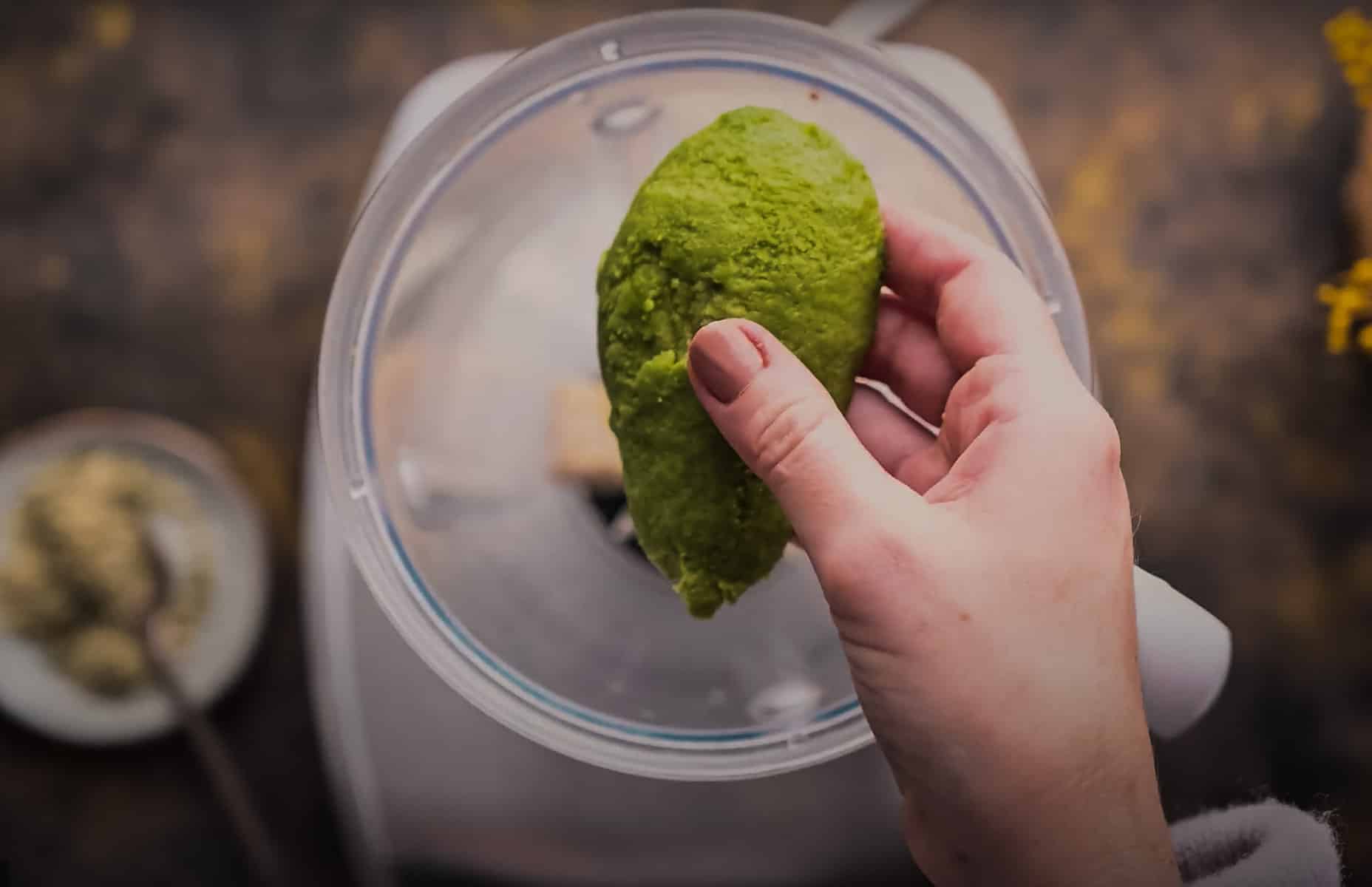 A person holds half of an avocado over a blender.