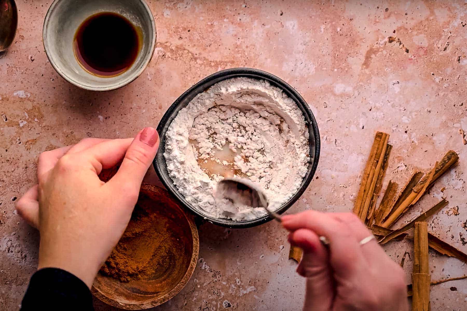 Hands holding a bowl of powdered sugar, mixing with a spoon. 