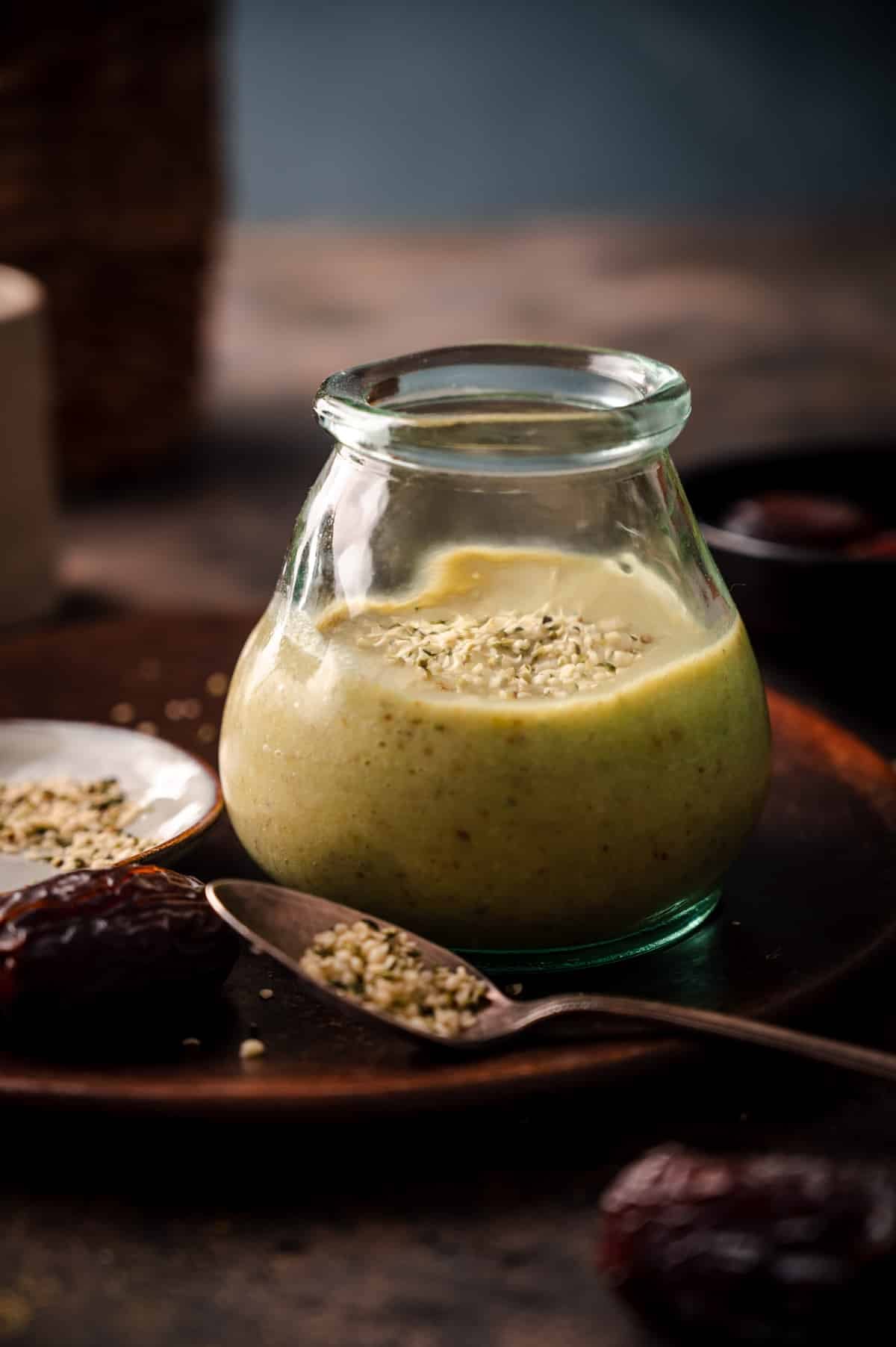 Fresh avocado smoothie in a clear glass cup on a plate with hemp seeds sprinkled on top.