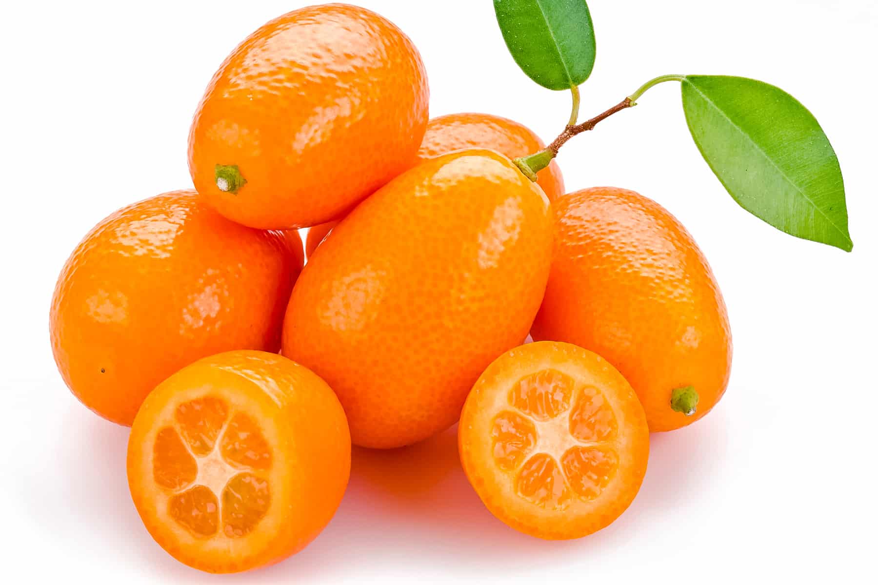 Small pile of kumquats with one cut in half showing its orange and white flesh.