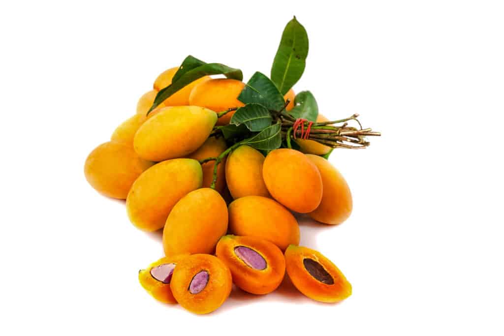 Several maprang fruit still on their branches bunched together with a few cut in half.