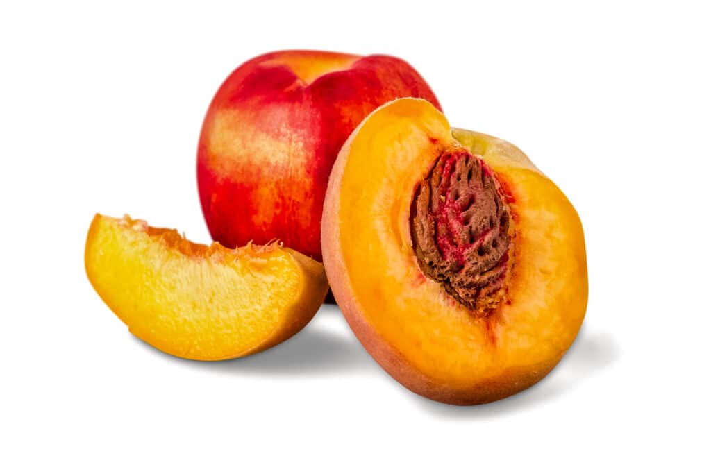 One large peach with another one cut open showing the stone (pit) and a slice.