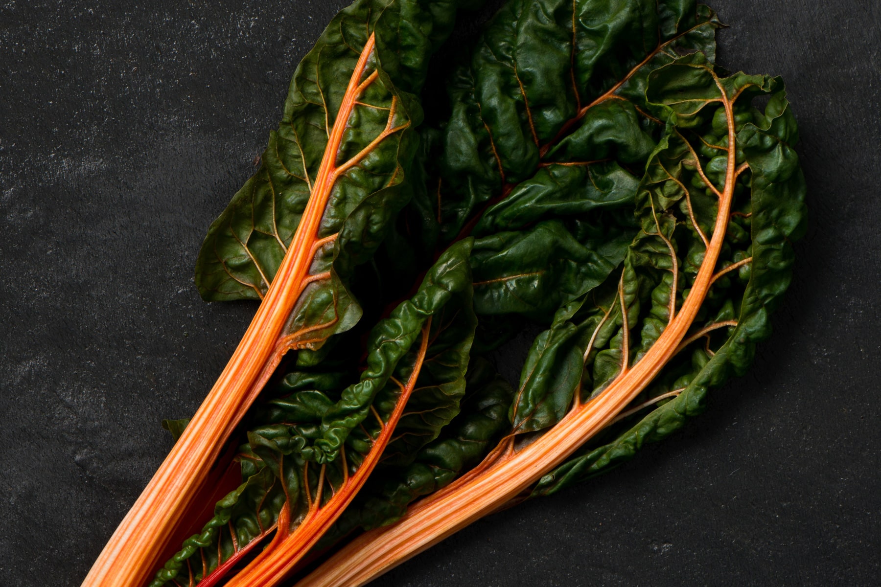 Three stalks of orange swiss chard on a black surface.
