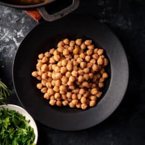 Close up of cooked chickpeas with fresh herbs on the side.