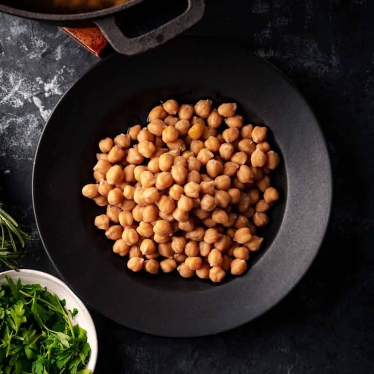 Close up of cooked chickpeas with fresh herbs on the side.