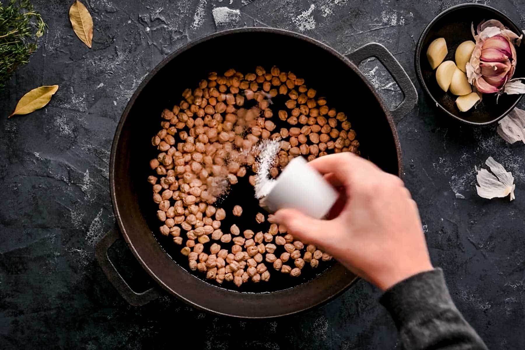Dried chickpeas in a black pot with salt being sprinkled on top.