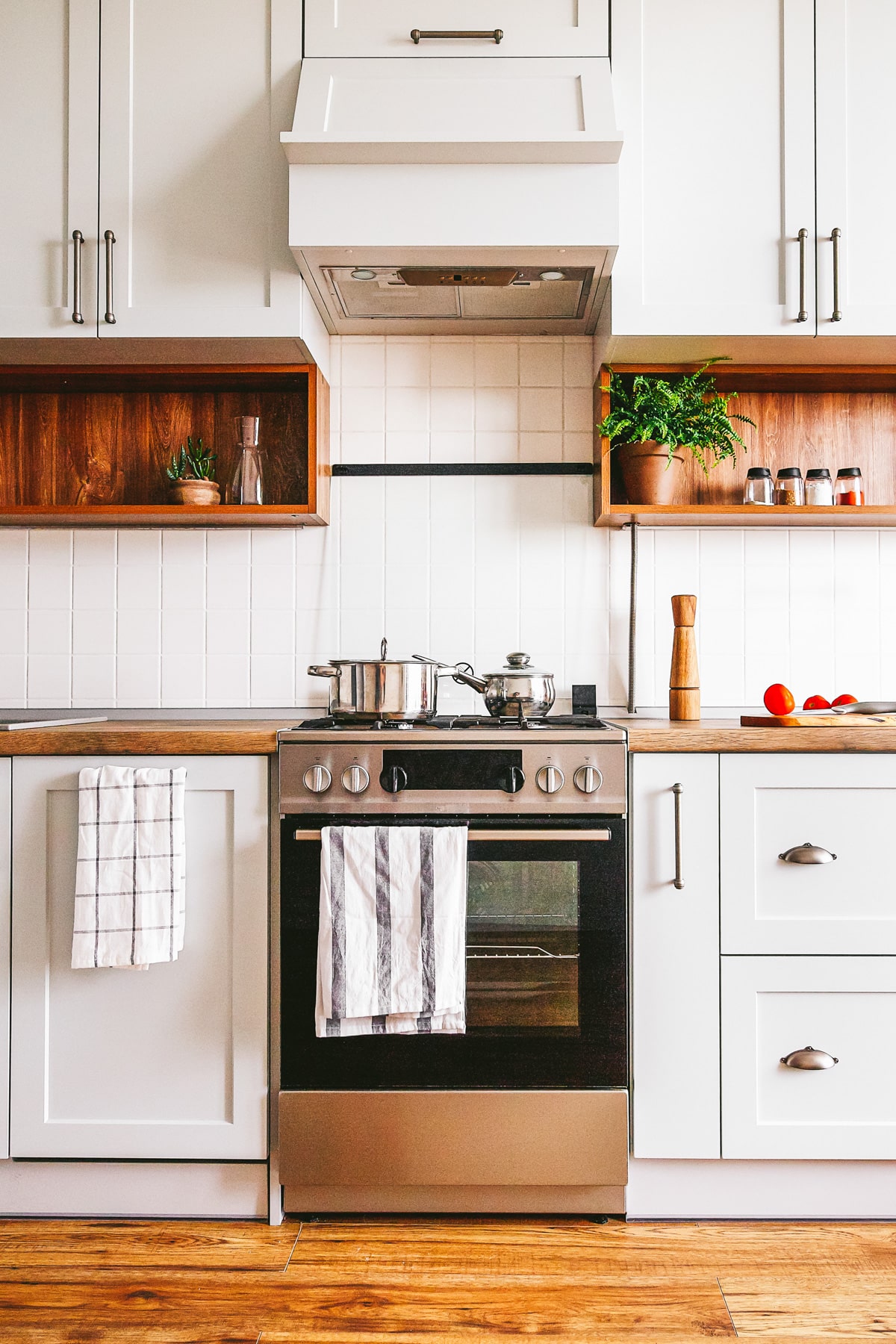 White Scandinavian style kitchen with stainless steel range and pots and pans on top.