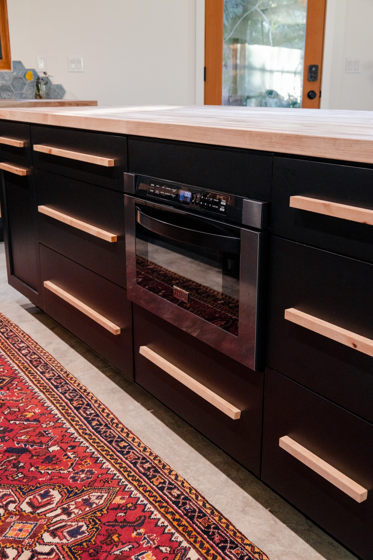 ZLINE black stainless steel microwave drawer inset into an island of black cabinets with a butcher block counter top. 