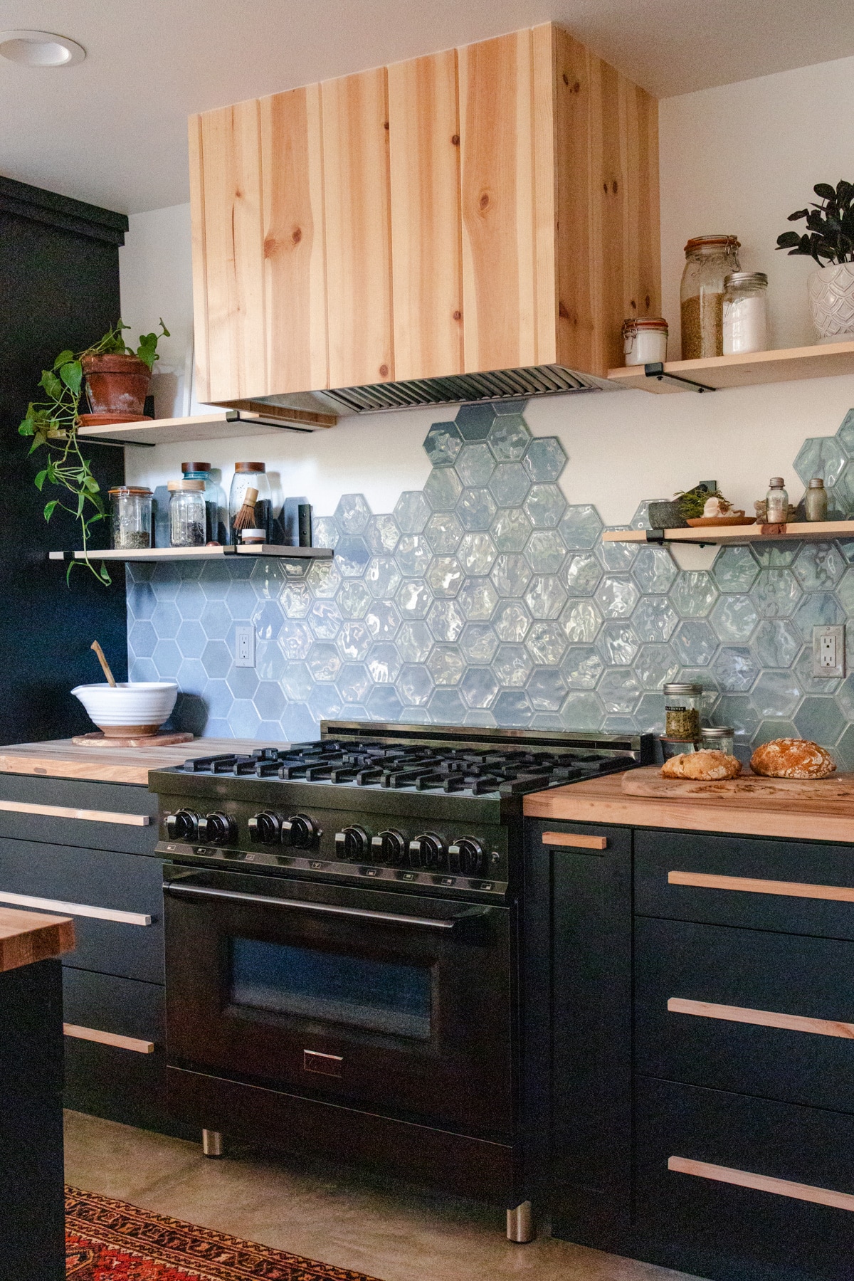 Thirty-six inch ZLINE black stainless steel gas range next to black cabinets and a stainless steel range hood insert.