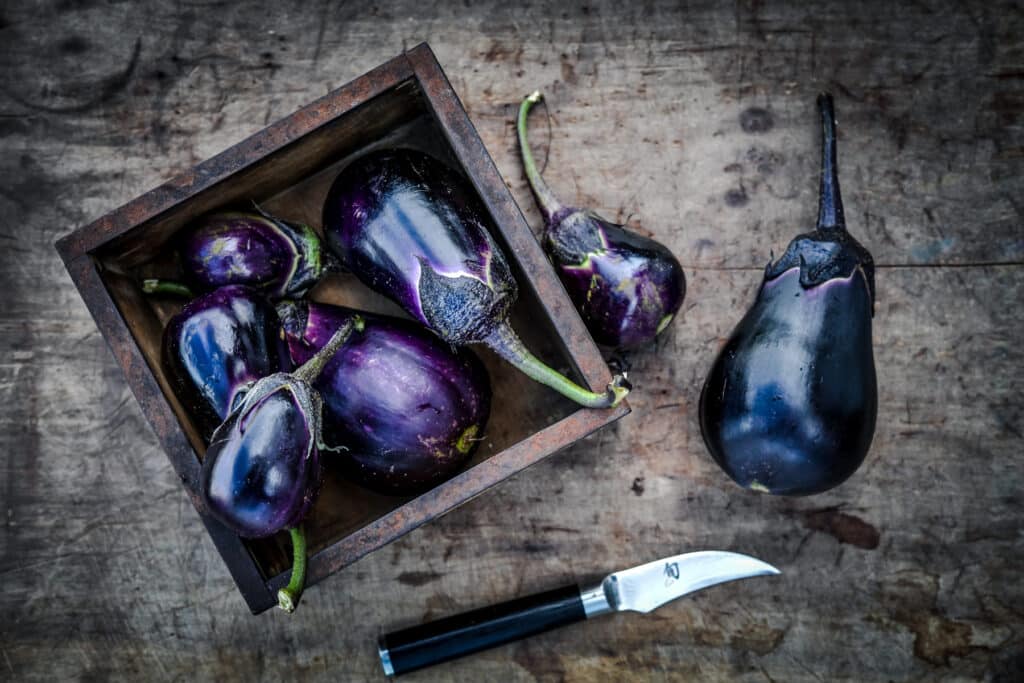 Senshu eggplant that's purple to black with black to green stems in a wooden box.