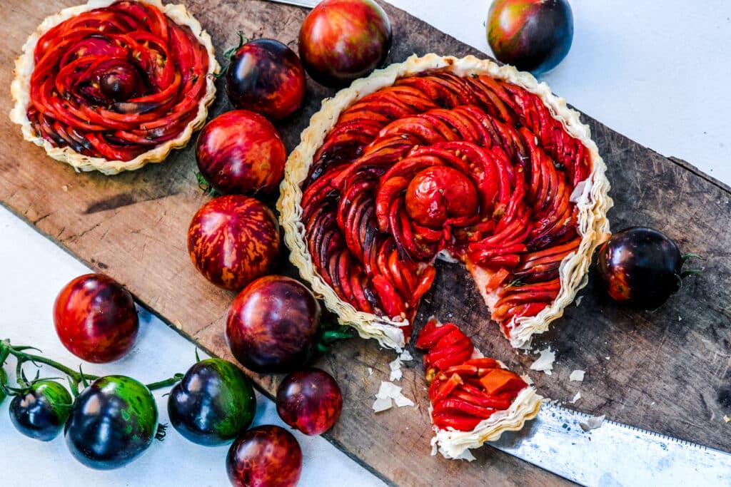 Queen of the knight tomato with black to red skin and a green stem next to a tomato tart.