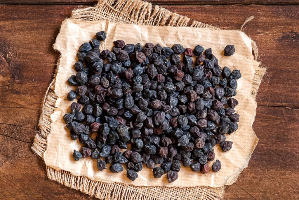 Black chickpeas on a piece of burlap across a wooden table.