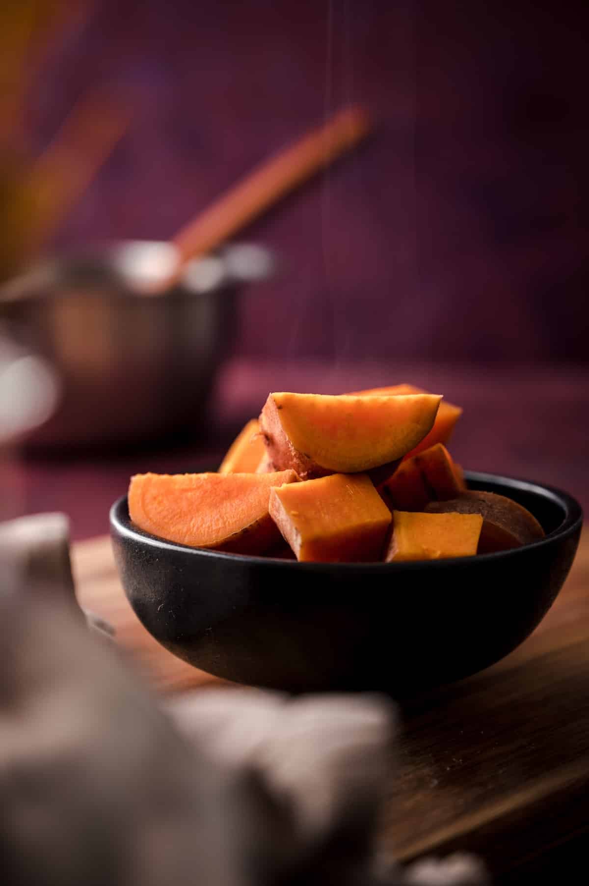 Steaming sweet potato chunks in a black ceramic bowl.