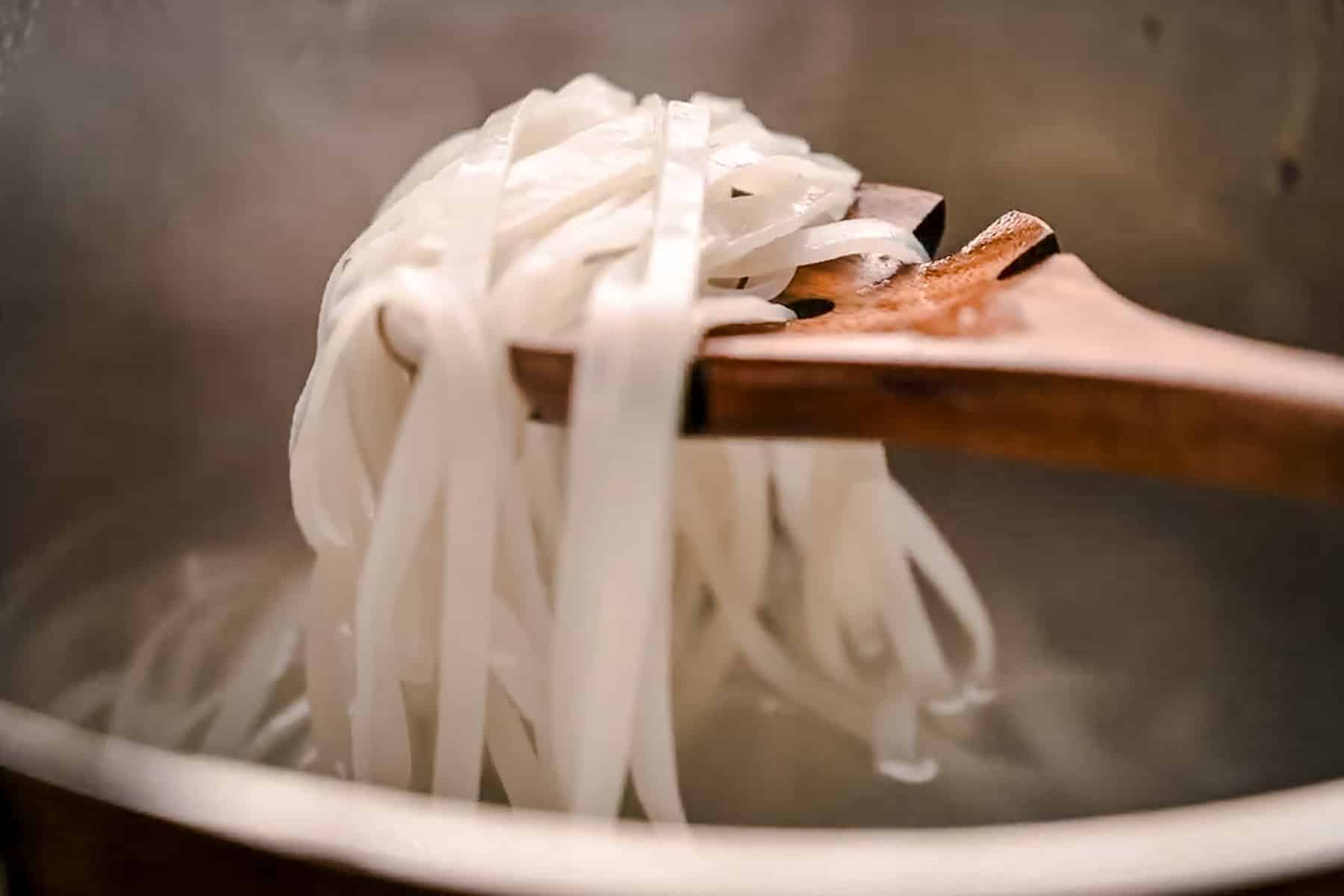 Wooden spoon scooping up a portion of cooked rice noodles.