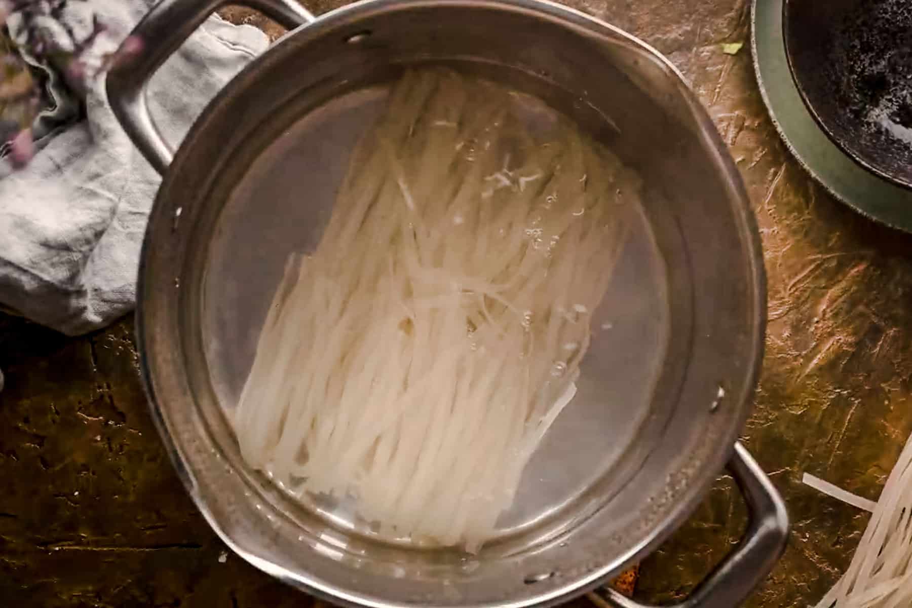 Rice noodles in a stainless steel pot of boiling water.