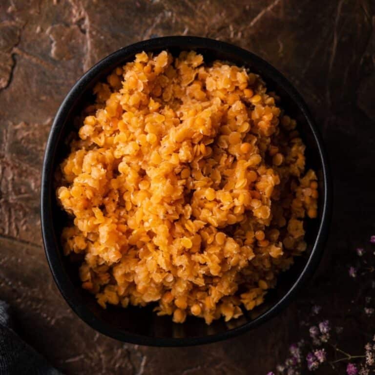 A black bowl filled with cooked, red lentils.