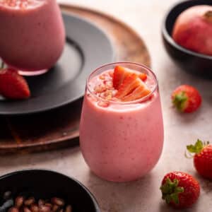 Light pink glass full of pomegranate smoothie topped with arils and strawberries.