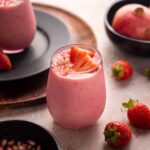 Light pink glass full of pomegranate smoothie topped with arils and strawberries.