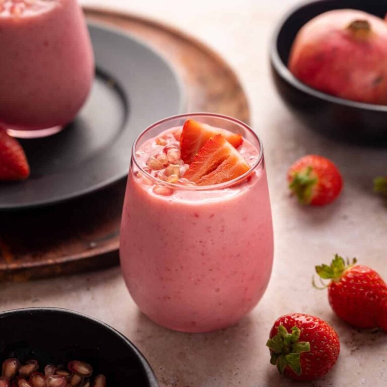 Light pink glass full of pomegranate smoothie topped with arils and strawberries.