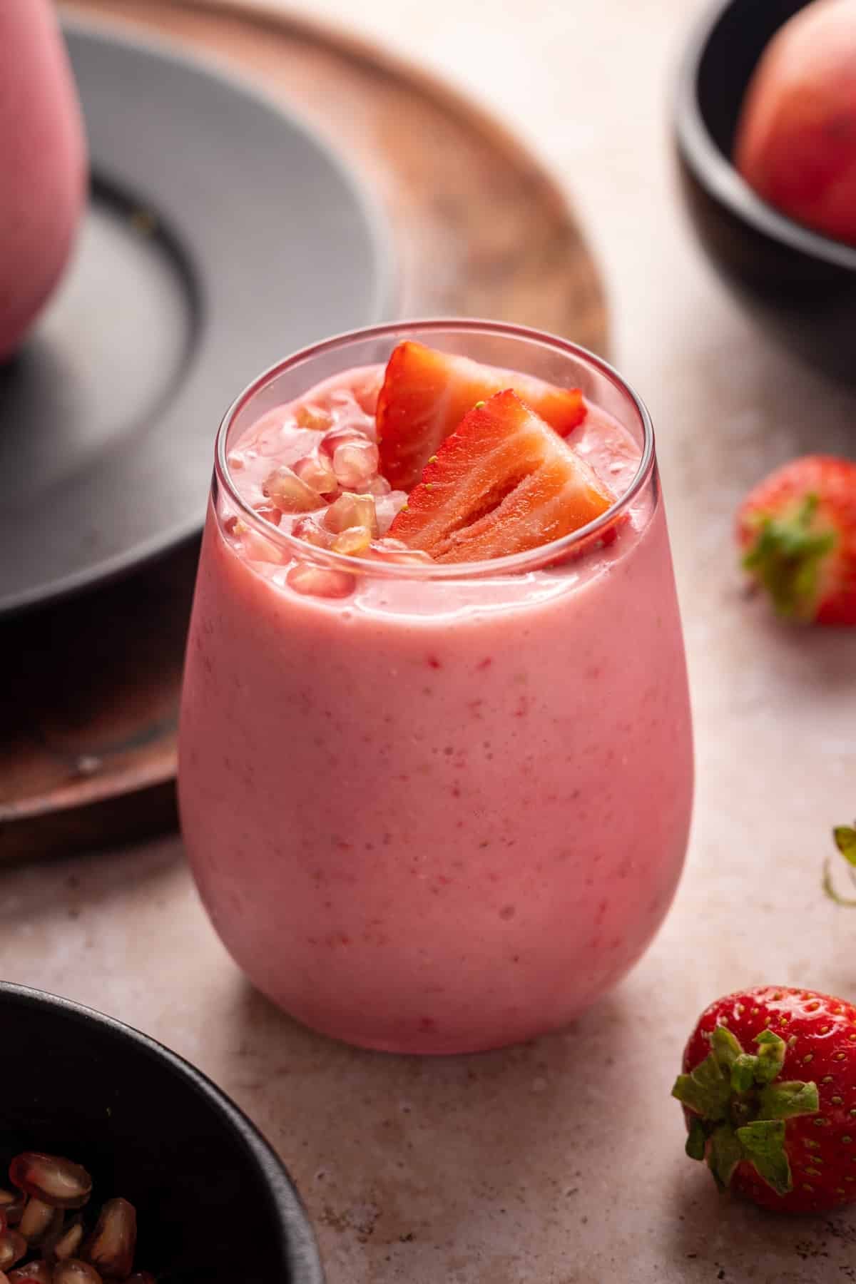Glass filled with pomegranate smoothie topped with sliced strawberries and pomegranate arils.