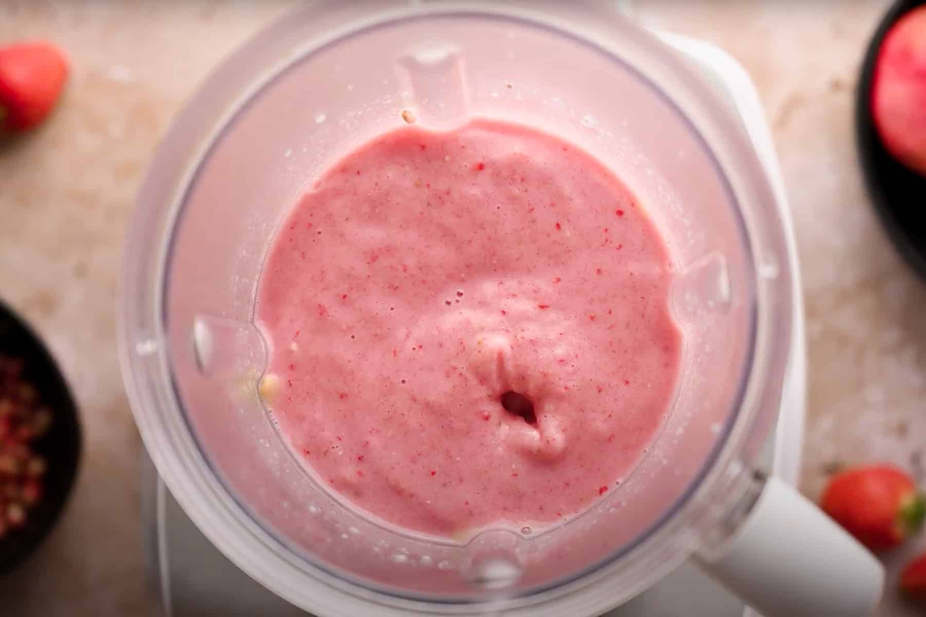 Top view of a blender filled with a smooth, pink strawberry and pomegranate smoothie. 