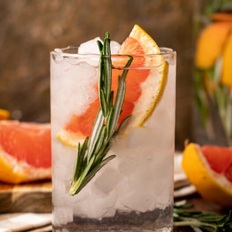 A glass filled with ice, grapefruit water, a grapefruit slice, and a sprig of rosemary.