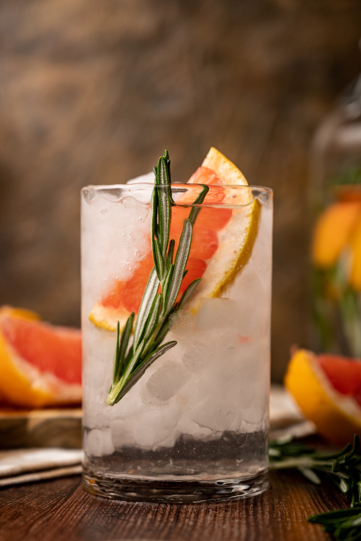 Glass of grapefruit water on a wooden table with pink grapefruit slices all around.