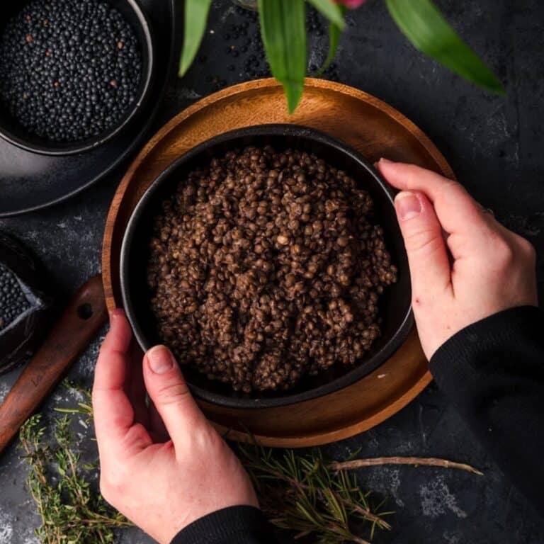 Hands holding a black bowl filled with cooked black lentils.