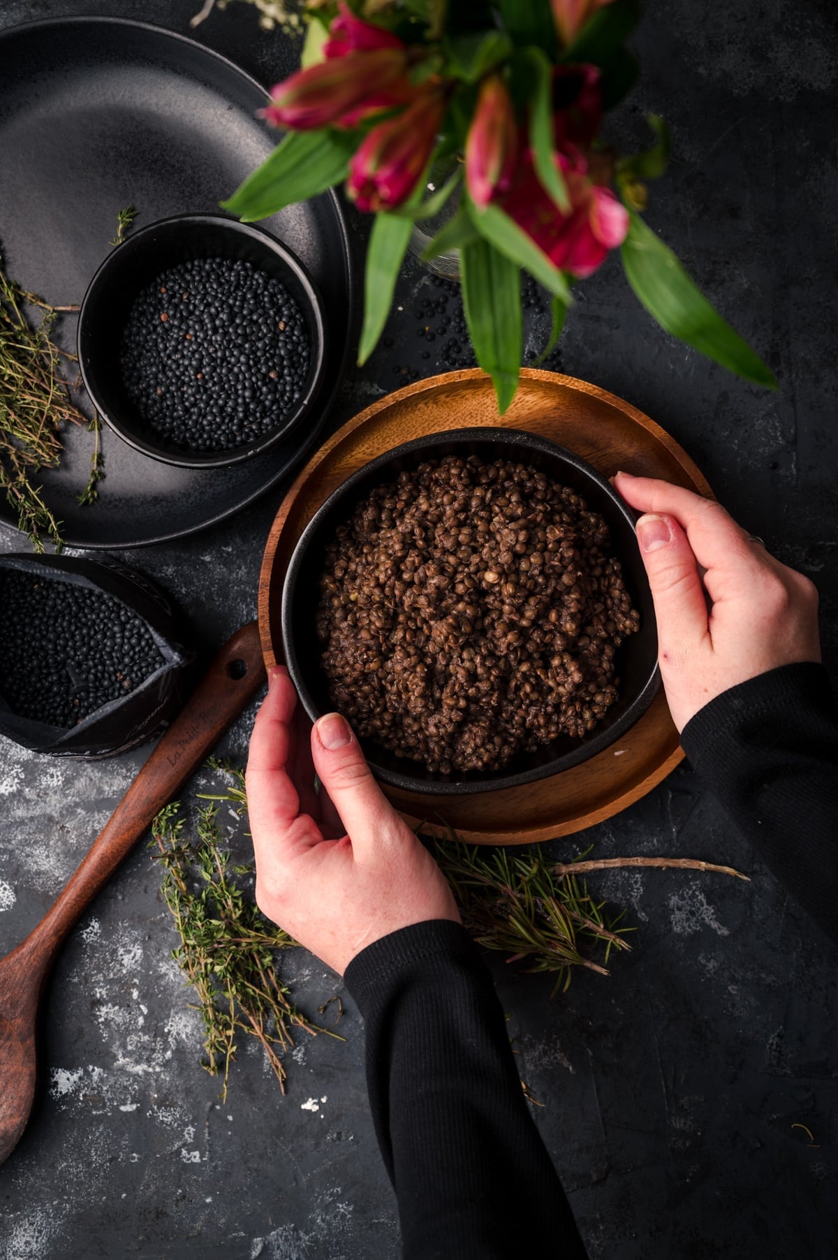 Woman reaching for and picking up black ceramic bowl filled with cooked black lentils.
