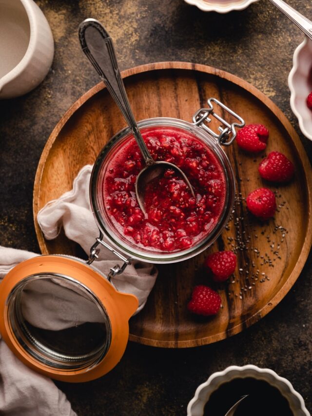 Raspberries in a jar on a wooden plate.
