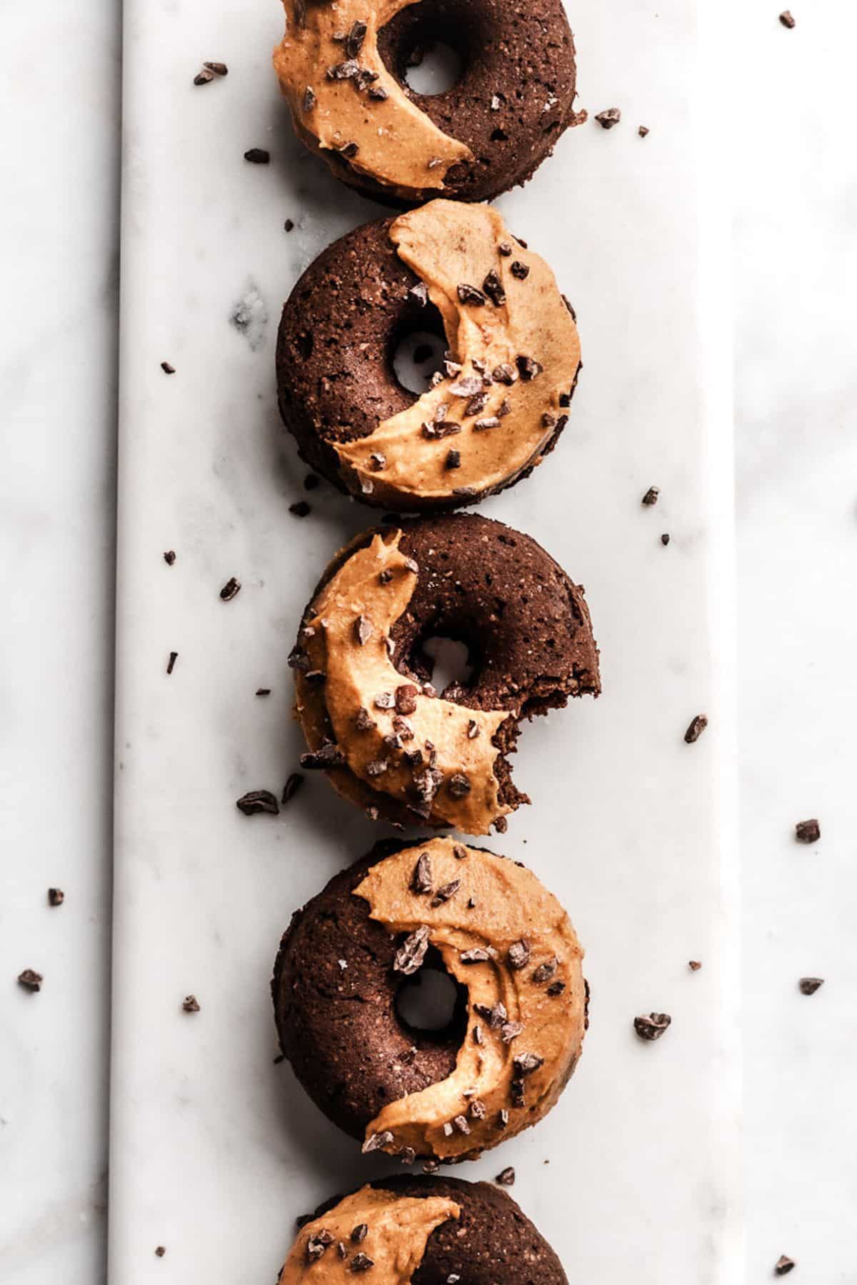 Chocolate baked donuts on a marble board in a straight line with pumpkin frosting on half of them.