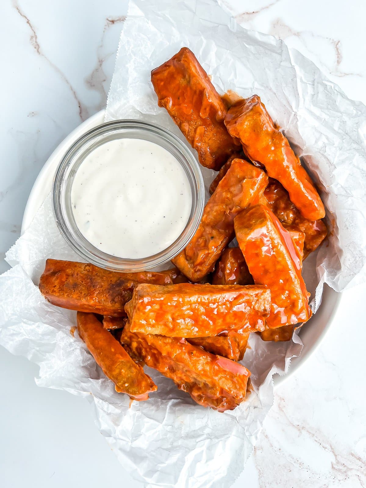 A bowl of vegan buffalo wings with a tofu-based dipping sauce.
