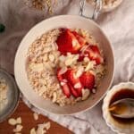 A large bowl of strawberry oatmeal with almonds and fresh strawberries on top.